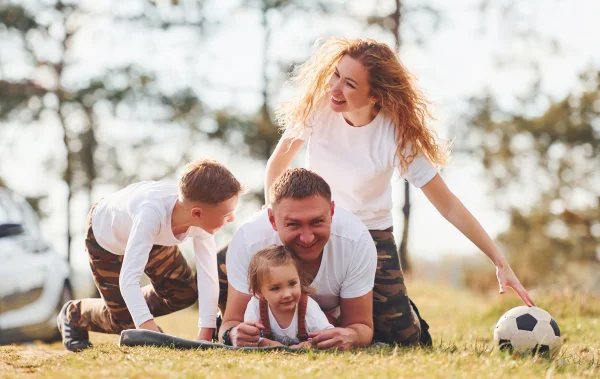 A picutre of a family in nautre having fun witha a soccer ball